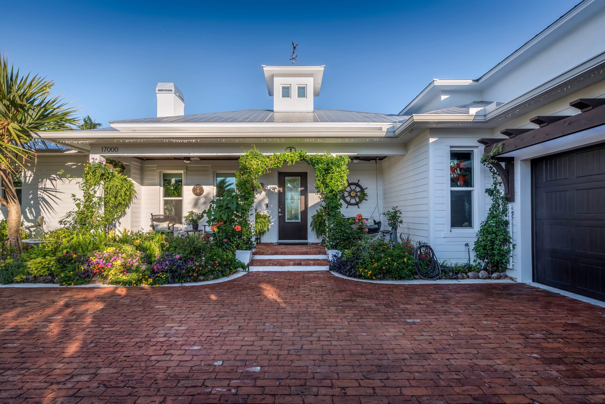 White Florida home with a metal roof, flowering front garden and brick driveway